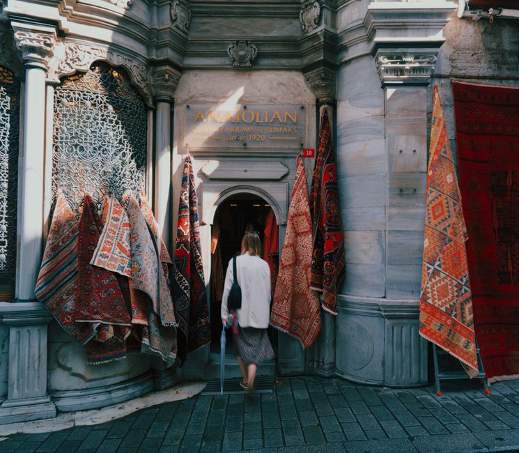 A woman enters a traditional carpet store in Istanbul, displaying vibrant Anatolian rugs.