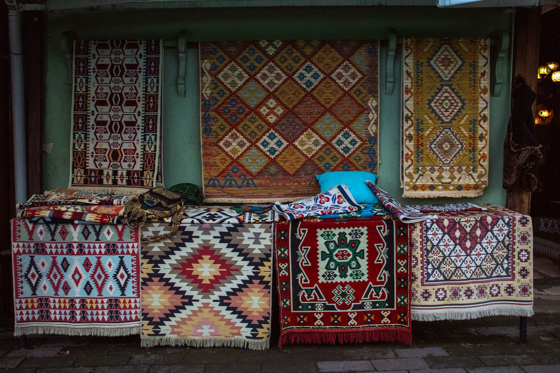 A vibrant collection of traditional woven rugs displayed outdoors in a market setting.