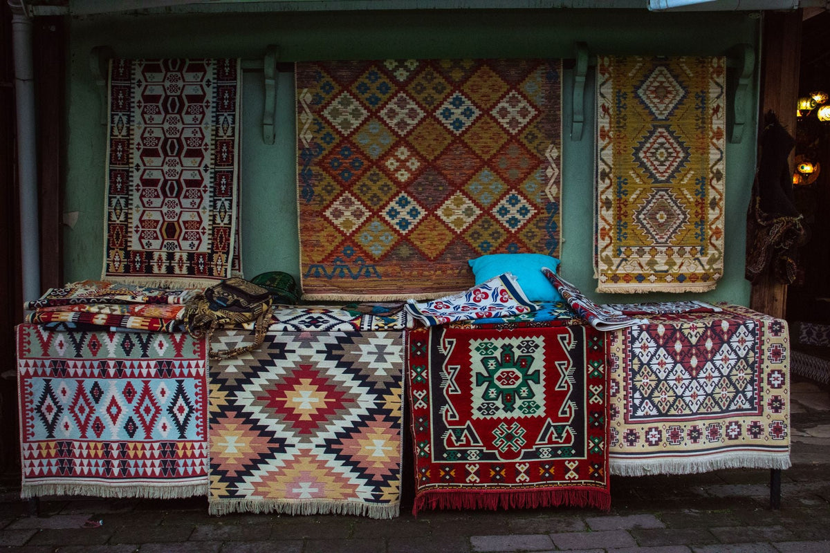 A vibrant collection of traditional woven rugs displayed outdoors in a market setting.