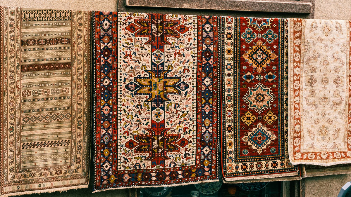 A vibrant array of vintage patterned rugs hanging outdoors, showcasing intricate designs and rich colors.