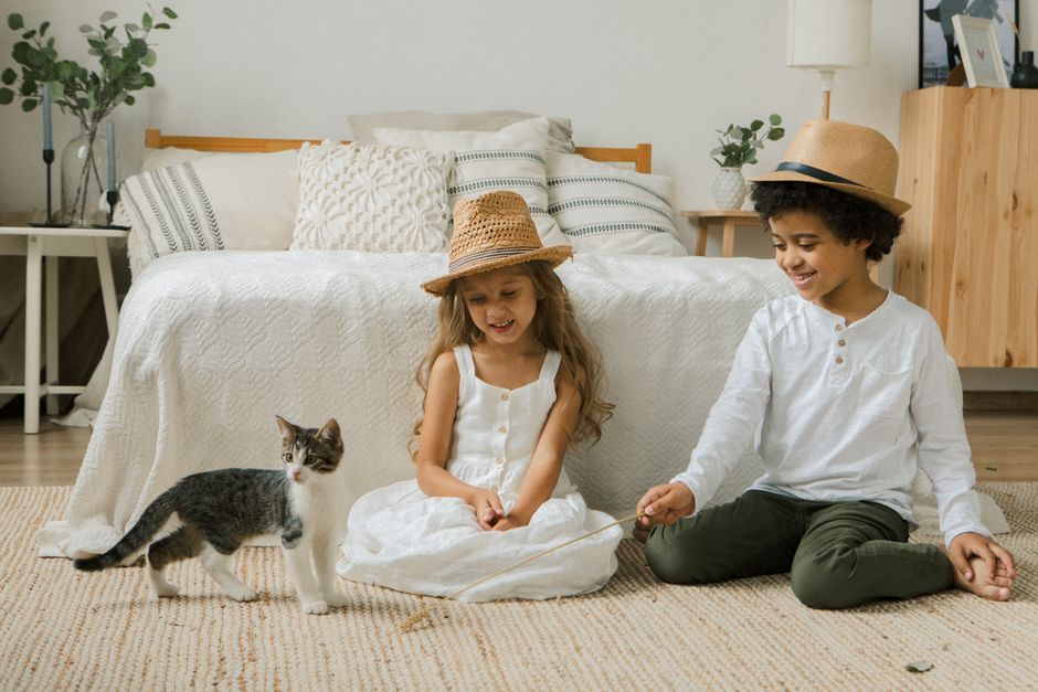 Two children in a bedroom enjoying playtime with a cute cat.
