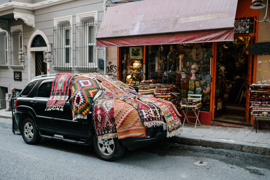 Vibrant Turkish carpets draped over a parked car in Istanbul street, showcasing local culture and craftsmanship.