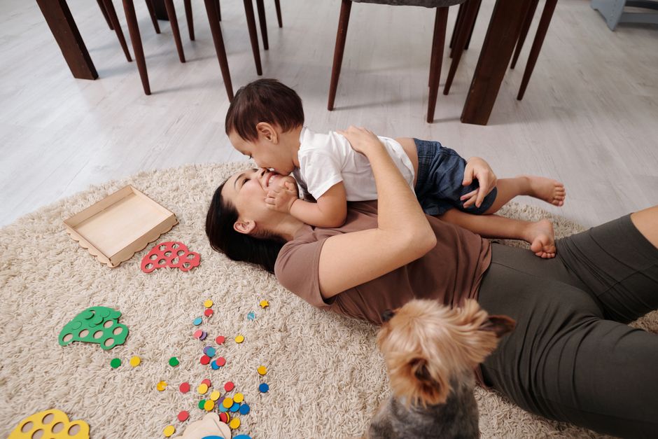 A joyful moment of a mother and toddler playing together indoors with their small dog.