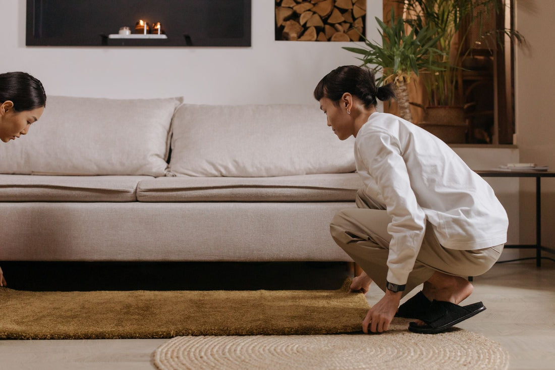 A couple arranging a rug in a stylish, cozy living room with elegant decor and plants.