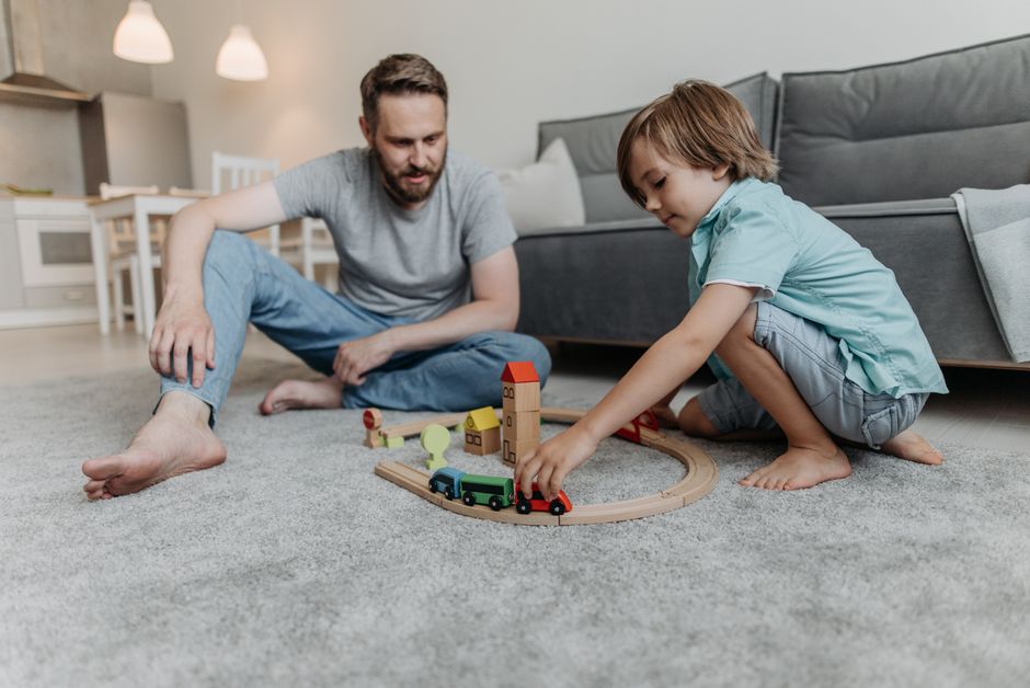 A father and son bond through playtime on the living room floor, enjoying wooden toys.